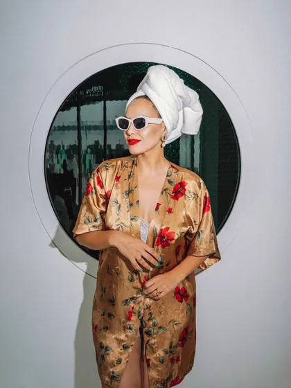 A stylish portrait of a model in a floral robe against a circular window. The composition is clean and modern, blending fashion with interior design elements.