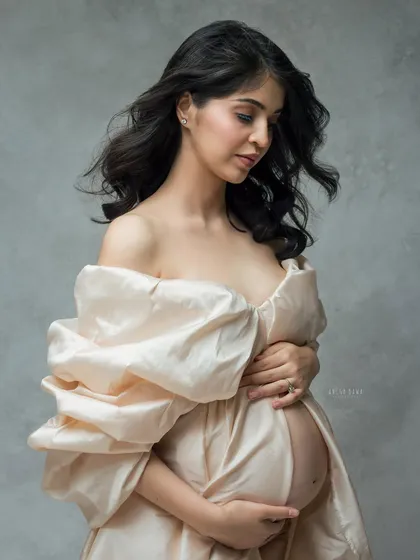 A close-up detail of the silk gown, focusing on the texture and the mother's gentle embrace of her bump. The wind in her hair adds a touch of life and movement.