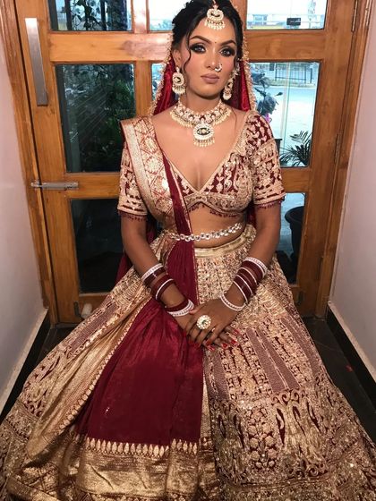 A full view of a bride in a maroon and gold velvet lehenga, a classic and regal choice for a winter wedding.