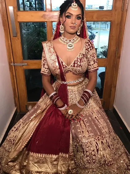 A full view of a bride in a maroon and gold velvet lehenga, a classic and regal choice for a winter wedding.
