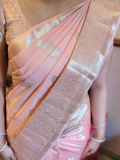 A soft pink silk saree draped to perfection. The focus is on the neat shoulder pleats and the clean lines of the pallu.