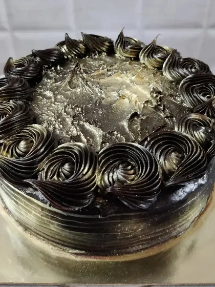 A chocolate cake with a stunning metallic gold and black finish. The piped rosettes add texture and elegance.