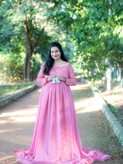 A classic outdoor portrait of a mom-to-be in a pink gown, holding a pair of tiny baby shoes.