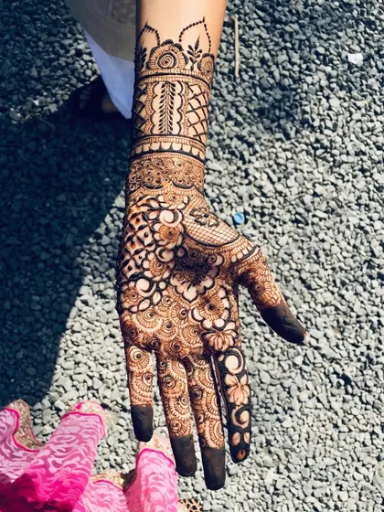 An intricate palm design for a bride, photographed in the sunlight. This pattern features a dense mix of jaal, floral, and paisley elements, with fully covered fingertips.