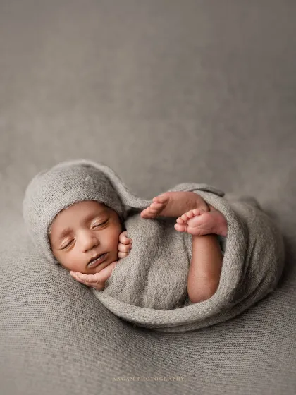 A classic "tucked in" pose using a simple grey wrap and bonnet. This pose is all about making the baby feel secure and womb-like.