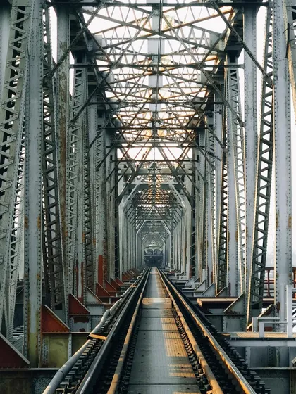 Looking down a long, symmetrical railway bridge. The repeating steel structures create a powerful leading line and a sense of infinite perspective, highlighting the beauty in industrial architecture.