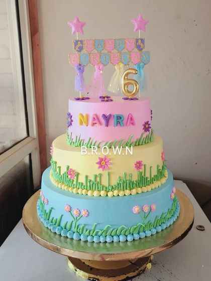 A three-tier cake with a spring meadow theme. The pastel layers are decorated with green grass and colorful flowers, creating a fresh and lovely design for a 6th birthday.