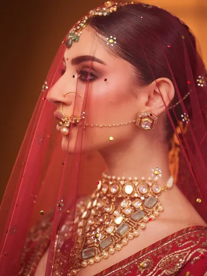 The beauty of a bride under her veil. This artistic shot highlights the eye makeup and the traditional nath.