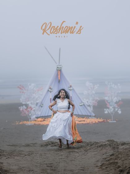 A joyful portrait of the bride running towards the camera during her beach Haldi, with a beautiful setup in the background.