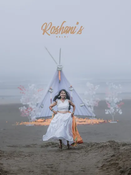 A joyful portrait of the bride running towards the camera during her beach Haldi, with a beautiful setup in the background.