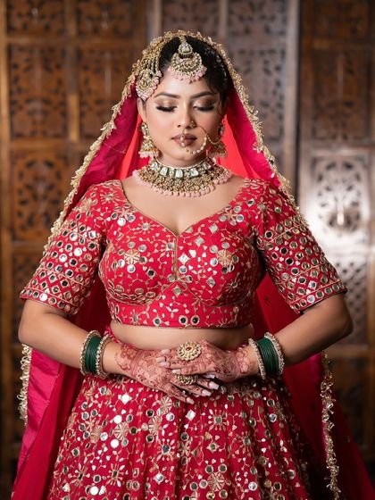 A bride in a red mirror-work lehenga, perfect for a sangeet or wedding. The mirror work catches the light beautifully.