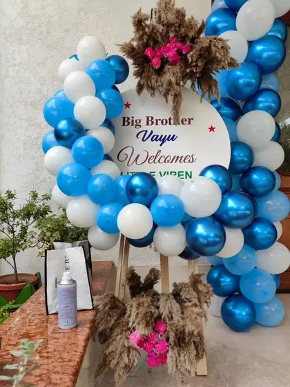 A sweet welcome sign for a new baby, announcing "Big Brother Vayu Welcomes Little Viren," framed by blue and white balloons.