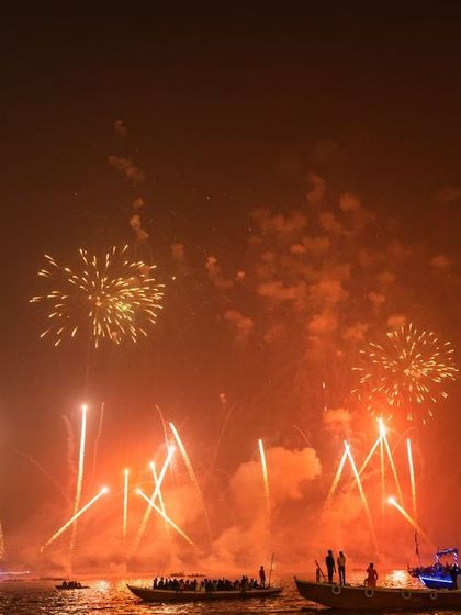 A massive fireworks display over the Ganga during Dev Deepawali. This shot captures the scale of the celebration, with boats full of spectators watching from the river.