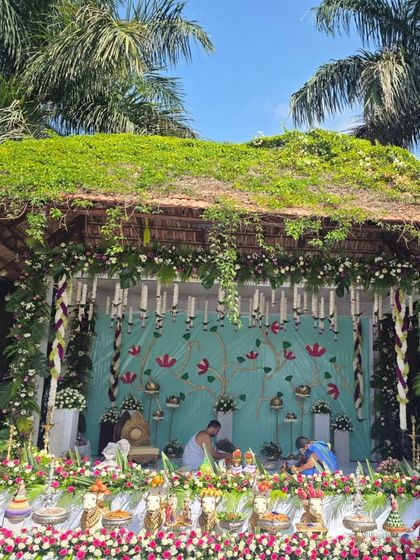 An outdoor naming ceremony setup under a thatched roof, with a beautiful turquoise backdrop and a full display of offerings.