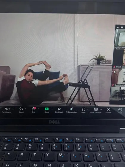 This is what our online classes look like. Even from your own home, you get detailed guidance. Here, a student uses a chair to deepen her hip opening pose, showing that a dedicated practice is possible anywhere.