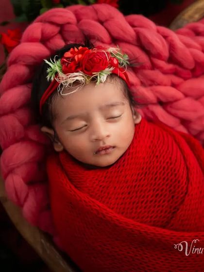 A close-up on the baby's face within the red theme. The delicate floral headband complements the bold red wrap, drawing attention to the baby's serene features.