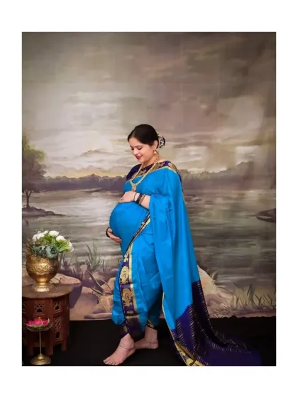 This profile shot beautifully highlights the baby bump, with the mother-to-be looking down with a gentle smile. The traditional saree and painted backdrop create a serene and classic portrait that feels both personal and artistic.