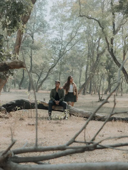 The couple takes a quiet moment on a fallen log in the middle of the forest. A serene and beautifully composed shot that speaks of peace and companionship.