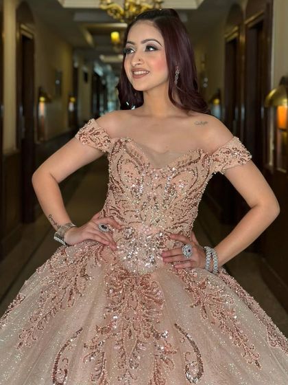 A client looking stunning in a glittery rose-gold Cinderella ball gown. The off-shoulder design and intricate sequin patterns create a look that is both romantic and glamorous.