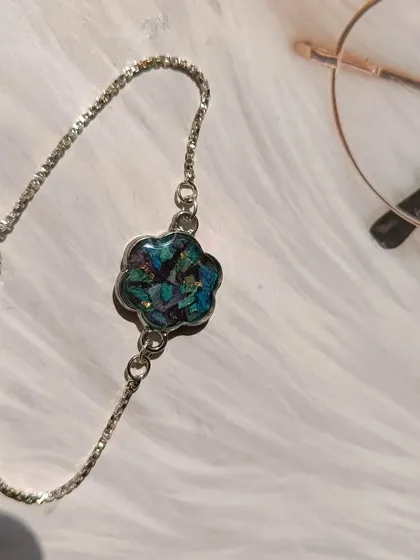 This image shows a beautiful bracelet made from preserved orchid petals. The silver flower-shaped setting perfectly complements the deep blue and purple of the petals.