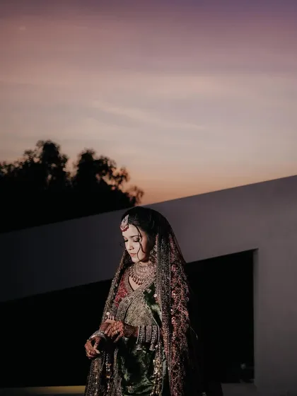 A stunning portrait of a bride in her intricate lehenga, captured against the soft colors of a sunset sky.