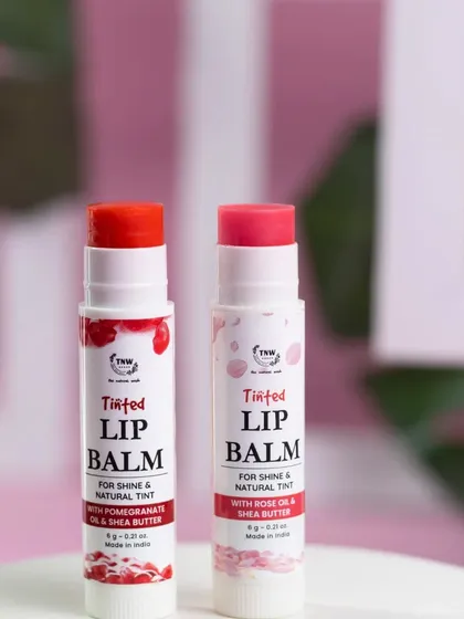 A simple, effective shot of two tinted lip balms against a soft pink and white background. The clean lines and minimal props make the products themselves the heroes of the image.