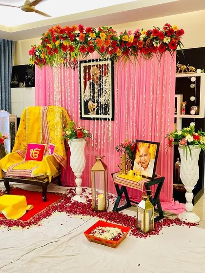 I create complete setups for Guruji satsangs at home. This one shows a main aasan with a yellow shawl, a pink curtain backdrop with a floral arrangement, and lanterns with rose petals for a blessed atmosphere.