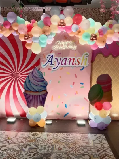 A fun and colorful Candyland theme for a 5th birthday. The setup includes backdrops with candy patterns, large cupcake and donut props, and a pastel balloon arch.