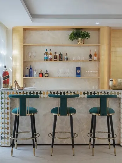 This bespoke home bar is where gold accents flirt with velvet green bar chairs. The bar front features a unique diamond-patterned inlay, creating a sophisticated spot for an evening pour.