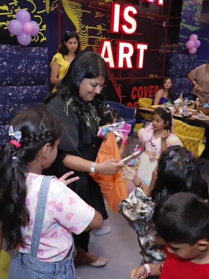 An adult hands out party favors to the kids. I help coordinate every part of the celebration, including the distribution of return gifts.