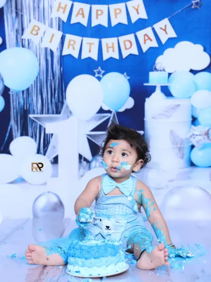 A baby boy enjoys his first taste of birthday cake during a fun and messy cake smash. The blue and white bear-themed outfit matches the festive party decorations perfectly.