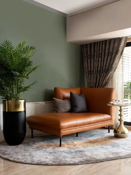 A cozy lounging corner featuring a tan leather chaise against a military green accent wall. This shows how I use color blocking and luxurious textures to create intimate, relaxing zones within a larger living area.
