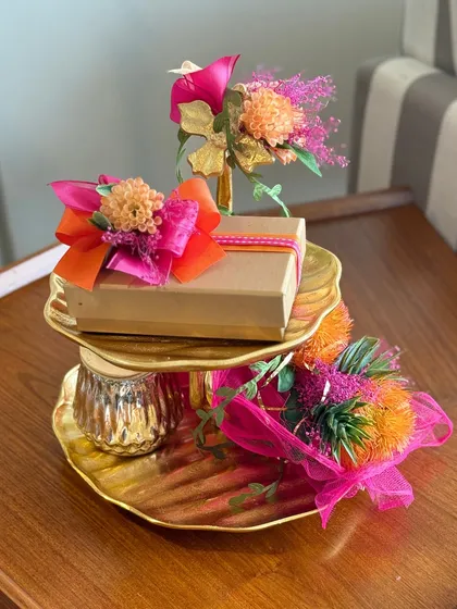 Our two-tiered golden platter is transformed into a vibrant Ganesh Chaturthi hamper, adorned with bright florals and a dry fruit box. It’s a gift that serves as a beautiful decor piece for the festive home.