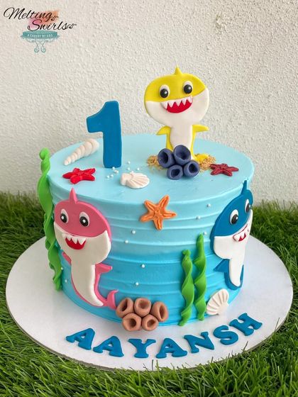 A simple yet adorable Baby Shark cake for a first birthday. This design uses handmade fondant sharks and sea elements on a blue whipped cream cake to create a fun underwater scene.