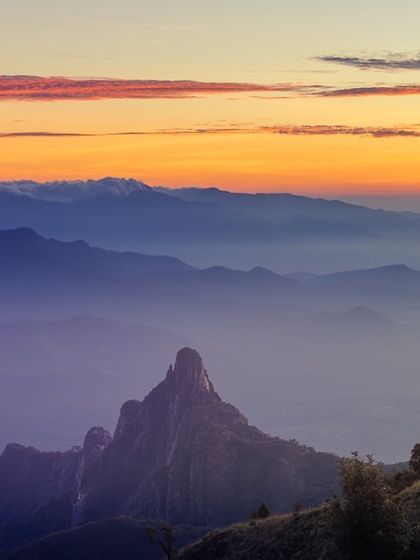 A close-up view of the unique, pointed shape of Rangaswamy Peak in the Nilgiris, shrouded in the purple and orange hues of dawn.
