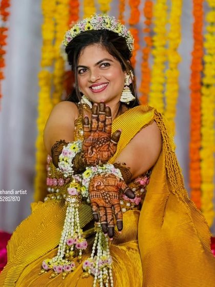 A joyful bride wearing a floral crown and jewelry, her hands beautifully adorned with my intricate henna work.
