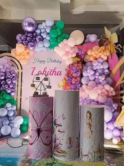 A magical fairy and butterfly garden theme for Lohitha's birthday. This enchanting setup uses a rich palette of purples, pinks, and greens, with fairy cutouts, butterfly wings, and custom-printed pedestals.