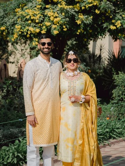 A stylish portrait of the couple at their Haldi ceremony. Wearing sunglasses and coordinated yellow outfits, they look cool, confident, and happy.