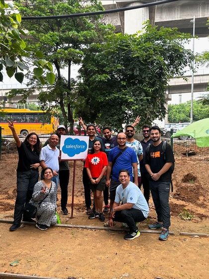 The Salesforce team poses with their company sign after a successful day of planting native species like Bistendu and Adusa at Aravali Creek.