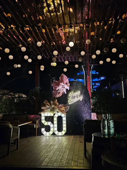 Celebrating a 50th birthday calls for something truly special. For this milestone party, I designed a sophisticated outdoor lounge setting with a dramatic sequin backdrop, a custom neon sign, and large marquee numbers, all under a canopy of warm string lights.