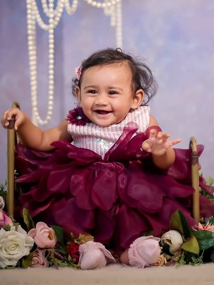 A beautiful floral swing setup. The baby is nestled in a seat surrounded by a cascade of pink and white flowers, with elegant pearls hanging from above, creating a soft and classic portrait.