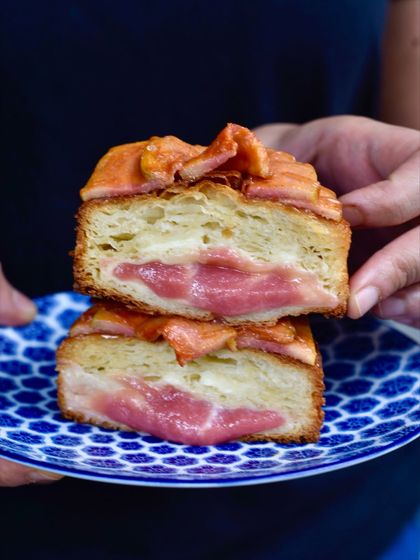 A cross-section of our Guava Kouign Amann, a laminated and caramelised croissant pastry. It's filled with a sweet custard and pink guava jam, then topped with fresh guava and a hint of chilli caramel.