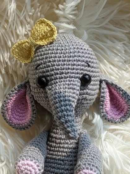 A close-up of the grey elephant with the yellow bow, showing her friendly, hand-stitched eyes.