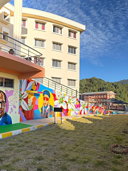 A wide shot of the 100-foot mural at St. Claret College, Ziro. The artwork spans the length of the building, featuring portraits of historical figures and colorful abstract designs that completely transformed the campus.