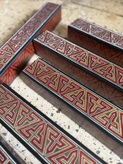 Wooden rafters hand-painted with intricate Arabic geometric patterns. Before installation, they are laid out, showing how each individual piece contributes to a larger, harmonious design.
