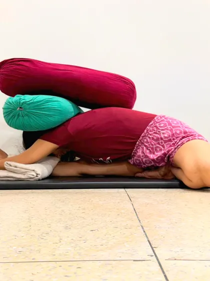 This is a restorative Janu Sirsasana with the support of multiple bolsters. Meditation is an introverting art. For those who are unstable, asana and pranayama are taught first to build strength in the nerves, senses, and mind, bringing balance before one moves to the inner layers of yoga.