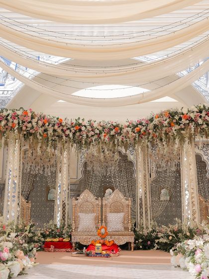 The mandap stage, set for the pheras. The design features traditional carved chairs against a backdrop of detailed thikri mirror work, all softened by a canopy of lush, pastel-toned florals.