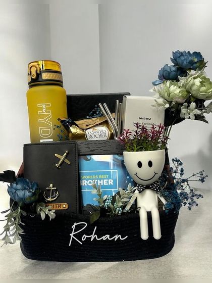 A personalized basket hamper for 'Rohan', filled with his favorite things including a travel-themed wallet, a water bottle, and a quirky planter, all in a stylish black and blue color scheme.