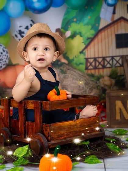 A little farmer in his hat, sitting in a wooden wagon in a fun farm-themed first birthday setup.