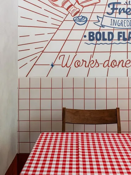 A detail of the graphic wall mural and custom seating at 'FLIP N FOLD'. The design combines playful typography with a classic red-and-white checkered tablecloth, capturing the fun and nostalgic spirit of an American diner.